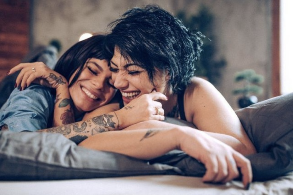 Two women smiling and cuddling in bed.